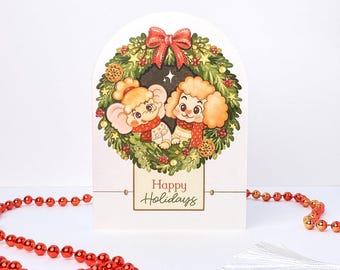 May include: An arched greeting card featuring a green Christmas wreath with a red bow, surrounding an illustration of a cartoon elephant and poodle wearing scarves. Below the wreath, a rectangular box contains the text Happy Holidays.