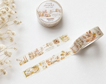 May include: A roll of washi tape labeled Cozy Autumn with a 15mm x 10m dimension, featuring illustrations of pumpkins, mushrooms, candles, and foliage in warm brown and orange tones, shown with a strip of the tape unrolled to display the pattern.