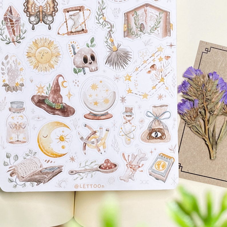 May include: A sheet of stickers featuring various illustrations in a whimsical style. The stickers include a witch's hat, a crystal ball, a moon, a sun, a butterfly, a book, a skull, a broom, a potion bottle, and more. The stickers are all in shades of brown, yellow, and white.