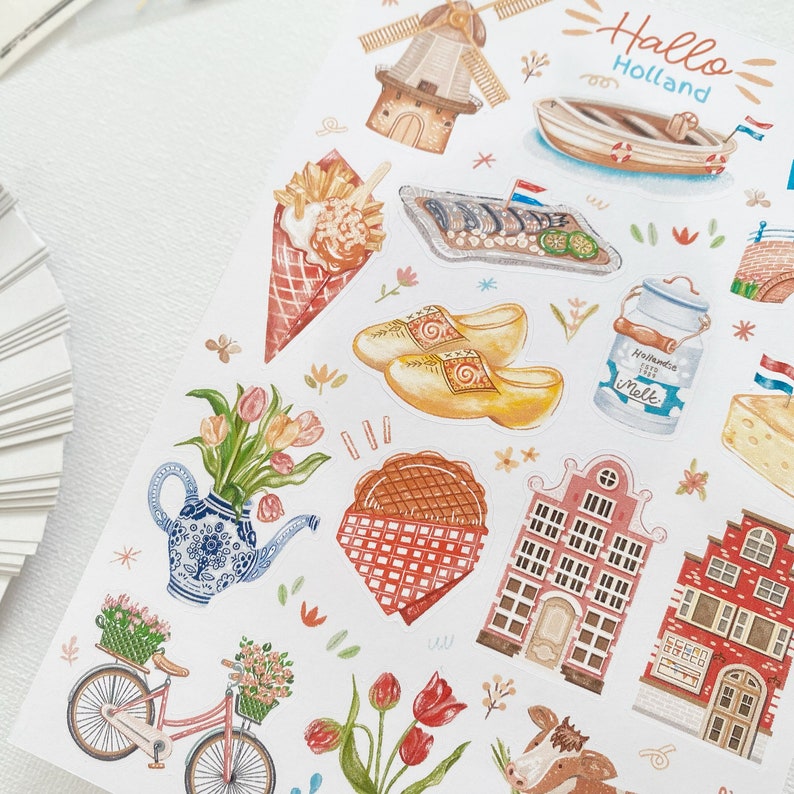 May include: A set of colorful stickers featuring Dutch themes, including a windmill, clogs, tulips, a canal house, and a milk jug. The stickers also feature the text "Hallo Holland".