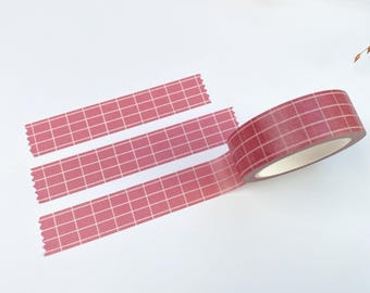 May include: A roll of adhesive washi tape featuring a dark red background with a white grid pattern. Three strips of the same tape are unrolled and laid out horizontally, showing the consistent grid design and the scalloped edge.