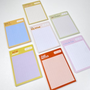May include: A collection of colorful sticky note pads with grid lines. Each pad has a different colored border and text, including "Bio Ideas," "Step 1 Write," "Now Never," "On My Mind," "Mission Impossible," "Totally Not A Secret Plan," and "Just Notes."