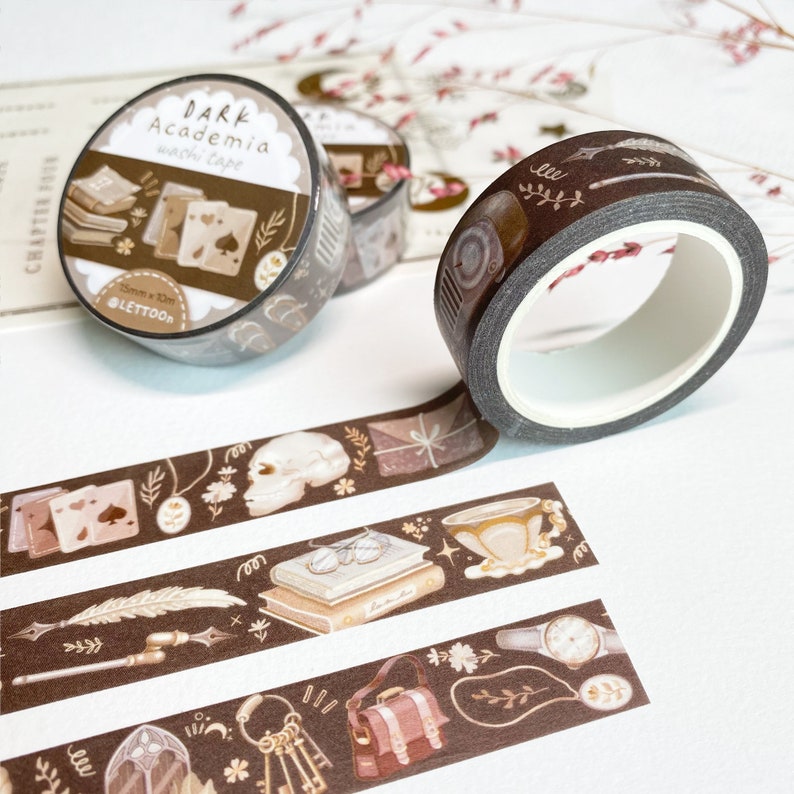 Peut inclure: Trois rouleaux de ruban adh&eacute;sif washi brun avec des illustrations de livres, de cl&eacute;s, d'un cr&acirc;ne, d'une plume, d'une tasse &agrave; th&eacute; et d'une montre. Le ruban est &eacute;tiquet&eacute; "DARK Academia washi tape" et "Lettoon".
