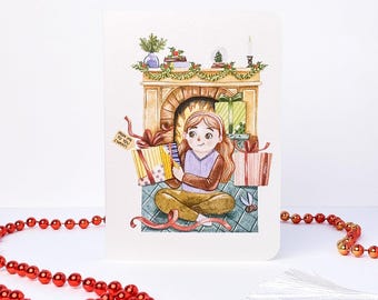 May include: A greeting card featuring a watercolor illustration of a person with long brown hair sitting on a floor in front of a fireplace, surrounded by wrapped gifts. The person holds a gift with a tag that reads FROM ME TO YOU (SURAY).