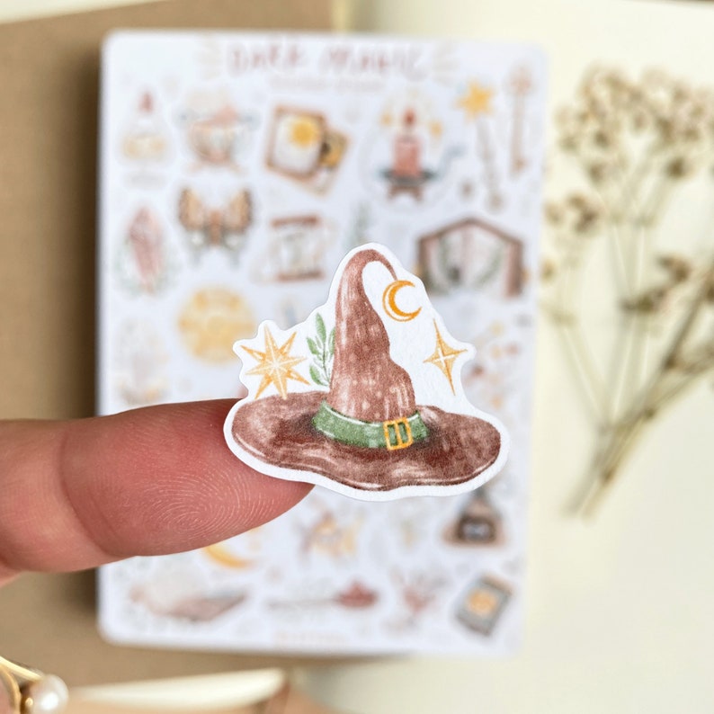 May include: A brown witch hat with a green band and a crescent moon on the top. The hat is decorated with gold stars and green leaves.