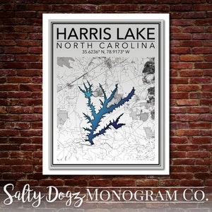 May include: A black and white map of Harris Lake in North Carolina with a blue and teal gradient fill. The map is framed in a white frame with a black border. The text "HARRIS LAKE NORTH CAROLINA 35.6236° N, 78.9173° W" is printed at the top of the map. The text "Salty Dogz MONOGRAM CO." is printed at the bottom of the map.