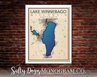 May include: A vintage-style map of Lake Winnebago in Wisconsin, with the lake highlighted in blue and the surrounding area in beige. The map includes the coordinates 44.0474° N, 88.4404° W. The text "Salty Dogz MONOGRAM CO." is at the bottom of the map.
