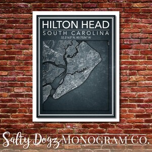 May include: A white framed print with a dark blue background featuring a map of Hilton Head, South Carolina. The text "HILTON HEAD" and "SOUTH CAROLINA" is printed in white above the map. The coordinates "32.2163° N, 80.7526° W" are printed in white below the map. The text "Salty Dogz MONOGRAM CO." is printed in white below the frame.