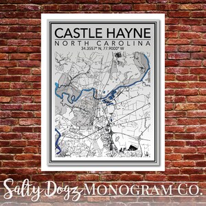 May include: A black and white map of Castle Hayne, North Carolina, with blue water features. The map is framed in a white frame and has the text "CASTLE HAYNE NORTH CAROLINA 34.3557° N, 77.9000° W" at the top. The text "Salty Dogz MONOGRAM CO." is at the bottom of the image.