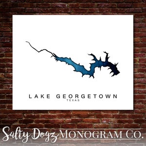 May include: A white print with a blue watercolor outline of Lake Georgetown, Texas. The text "LAKE GEORGETOWN TEXAS" is below the outline. The text "Salty Dogz MONOGROM CO." is at the bottom of the print.