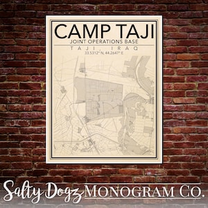 May include: A framed map print of Camp Taji, Joint Operations Base in Taji, Iraq. The map is in a neutral color palette with black text that reads "CAMP TAJI" and location coordinates. The print is displayed against a red brick wall.