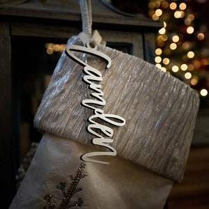 May include: A white stocking with a silver glitter cuff and a wooden name tag that says "Camden".