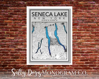 May include: A black and white map of Seneca Lake, New York, with the lake highlighted in blue. The coordinates 42.6918° N, 76.9202° W are printed below the lake. The text "SENECA LAKE" and "NEW YORK" are printed above the map. The text "Salty Dogz MONOGRAM CO." is printed below the map.