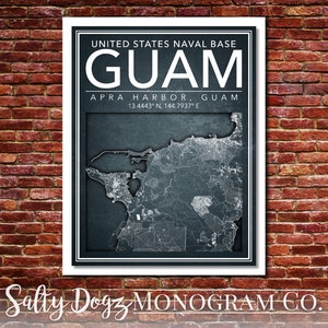 May include: A black and white map of Guam with the text "UNITED STATES NAVAL BASE GUAM" and "APRA HARBOR, GUAM 13.4443° N, 144.7937° E" printed on a white background. The map is framed with a white border.