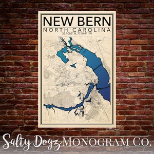 Puede incluir: Una impresión de mapa de estilo vintage de New Bern, Carolina del Norte, con una característica de agua azul. El mapa está enmarcado y tiene el texto "NEW BERN NORTH CAROLINA 35.1085° N, 77.0441° W Salty Dogz MONOGRAM CO." impreso en él.