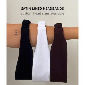 Op de afbeelding: Drie met satijn gevoerde haarbanden in zwart, wit en bruin. De haarbanden worden op een arm getoond, waarbij hun kleuren en ontwerp worden getoond. De tekst bovenaan luidt "SATIN LINED HEADBANDS custom head sizes available."