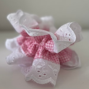 Könnte beinhalten: Ein rosa-weißes Gingham-Haargummi mit weißem Häkelspitzenbesatz.
