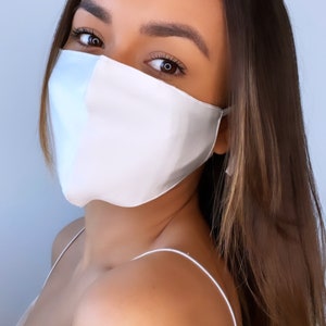 Puede incluir: Una mujer con una mascarilla facial de satén blanco. La mascarilla le cubre la nariz y la boca. Tiene el pelo largo y castaño y mira a la cámara.