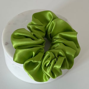 May include: A bright green satin scrunchie, a hair tie, on a white background.
