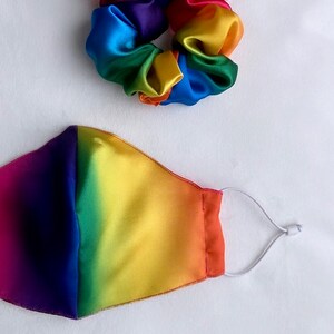 May include: A rainbow-colored satin scrunchie and a rainbow-colored face mask with a white elastic band.