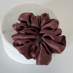 Può includere: Un elastico per capelli in raso marrone, su una superficie di marmo bianco.