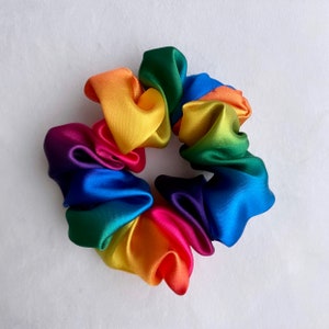 May include: A rainbow-colored satin scrunchie with a bright yellow, orange, red, purple, blue, green, and yellow color scheme.