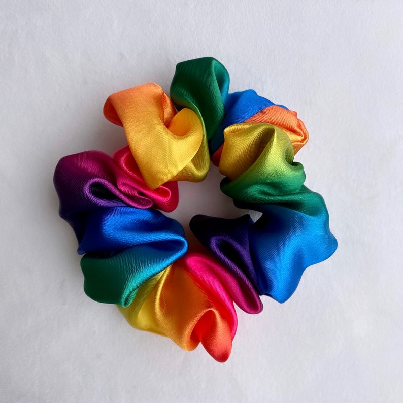 May include: A rainbow-colored satin scrunchie with a bright yellow, orange, red, purple, blue, green, and yellow color scheme.