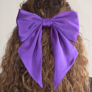 Könnte beinhalten: Eine große violette Schleife aus Satin mit einer Knotenmitte. Die Schleife ist in einer Frisur gebunden.