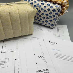 Puede incluir: Dos estuches de tela con cierres de cremallera y un patrón de costura. Uno es amarillo claro con un estampado floral y un diseño acolchado. El otro es blanco con diseños de árboles azules y un volante de cuadros amarillos.