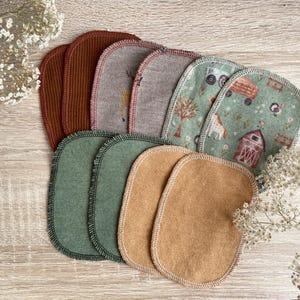 Könnte beinhalten: Ein Set aus acht ovalen Stoff-Patches in verschiedenen Farben und Mustern. Die Patches sind aus verschiedenen Materialien gefertigt, darunter Cord, Filz und bedruckte Baumwolle. Die Patches sind alle etwa 10 cm lang und 5 cm breit.