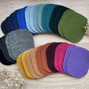 Könnte beinhalten: Eine Sammlung von Filz-Kreisen in verschiedenen Farben, darunter Blau, Grün, Lila, Braun und Gelb. Die Kreise sind in einer Halbkreisform angeordnet, wobei die dunkleren Farben links und die helleren Farben rechts liegen.