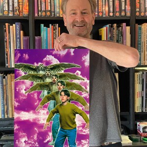 May include: A man holds a poster with a purple background and clouds. The poster features a young boy in a green shirt and blue jeans standing in front of a group of owls with their wings spread.