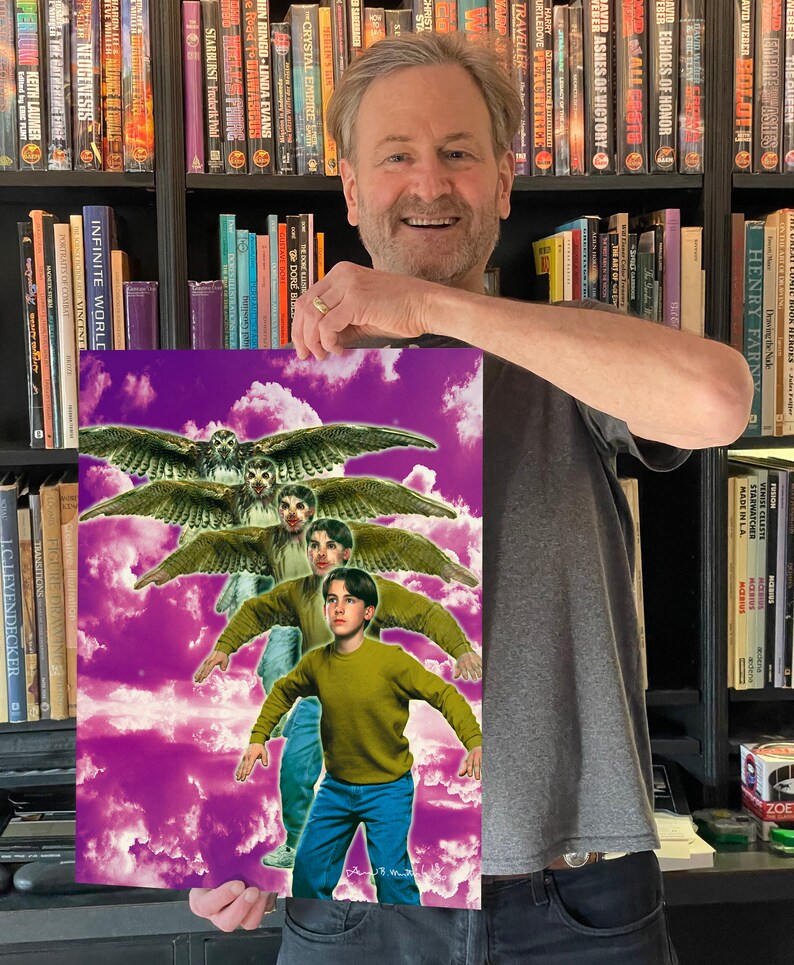 May include: A man holds a poster with a purple background and clouds. The poster features a young boy in a green shirt and blue jeans standing in front of a group of owls with their wings spread.