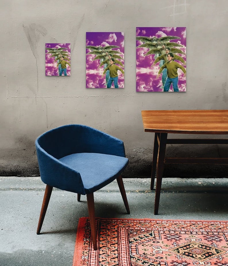May include: Three framed prints of a person flying with wings against a purple and white cloudy background. The prints are different sizes and are hanging on a gray wall. A blue chair and a wooden table are in the foreground.