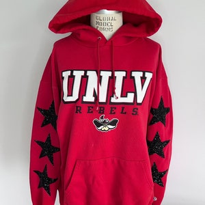May include: Red hooded sweatshirt with UNLV Rebels logo and black glitter stars on the sleeves.