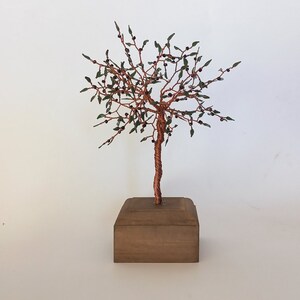 May include: A small copper wire tree sculpture with green leaves and a brown wooden base.