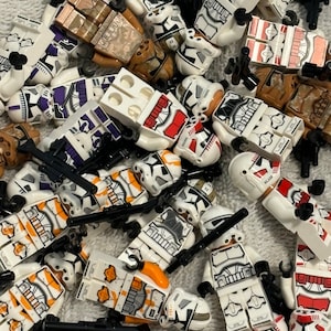 May include: A collection of white, orange, red, and purple Lego minifigures of clone troopers. The minifigures are all in different poses and have different weapons and accessories.