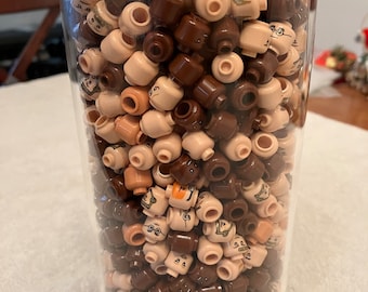 May include: A clear glass jar filled with a variety of brown and tan Lego minifigure heads. The heads have different facial expressions and hairstyles.