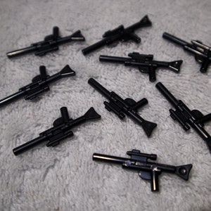 May include: A collection of eight black plastic toy blasters, resembling futuristic weapons. The blasters have a variety of designs and details, including scopes, barrels, and handles.