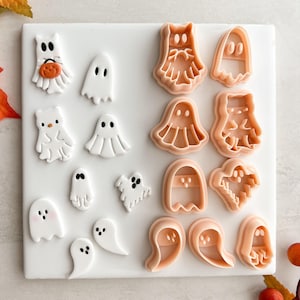 May include: A selection of Halloween-themed cookie cutters and fondant decorations. The image shows various ghost designs, including cartoon ghosts and ghost-shaped cutters in a light orange colour. The decorations are white and the background is white.
