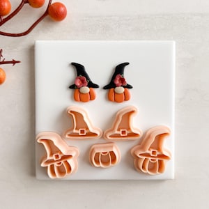 May include: A collection of Halloween-themed cookie cutters and decorative figures. The set includes two gnome figures with orange pumpkin bodies, black witch hats, and floral accents. Also included are hat and pumpkin-shaped cutters.