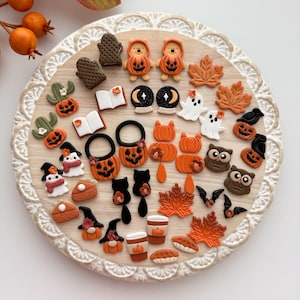 Puede incluir: Una colección de adornos decorativos con temática de Halloween, que incluye calabazas, fantasmas, búhos y murciélagos. El surtido presenta varios colores y diseños, dispuestos sobre una bandeja circular de madera con borde decorativo.