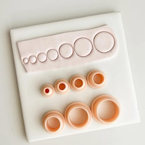 May include: A collection of pink circle-shaped cookie cutters of varying sizes, arranged on a white surface. The cutters are made of a soft, flexible material and are designed for use in baking or crafting. The image shows the cutters in different sizes.