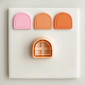 Könnte beinhalten: Vier farbige Ausstecher in Form von Bogenfenstern. Die Farben sind Rosa, Orange und Pfirsich. Der Fenster-Ausstecher hat ein Kreuzdesign im Inneren. Diese Ausstecher werden wahrscheinlich zum Backen und Dekorieren von Keksen verwendet.