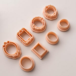 May include: A collection of peach-colored cookie cutters in various shapes, including circles, ovals, and squares. Some cutters have decorative edges, while others are plain. These tools are ideal for baking and crafting.