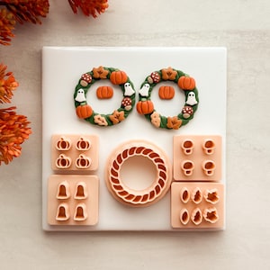 May include: Two circular wreaths decorated with miniature clay pumpkins, ghosts, mushrooms, and leaves, accompanied by five peach-colored plastic cutters featuring shapes of pumpkins, ghosts, mushrooms, leaves, and a braided wreath frame.