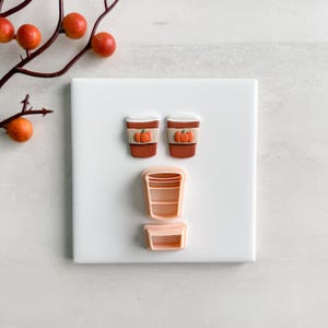 以下が含まれることがあります： 秋をテーマにしたクッキーカッターのコレクション。カボチャのデザインの茶色のコーヒーカップカッター2つと、コーヒーカップの形と長方形の2つの薄いピンクのカッター。