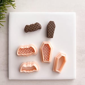 May include: A collection of Halloween-themed cookie cutters. The set includes a bat and coffin-shaped cutters in brown and a set of bat and coffin-shaped cutters in peach.