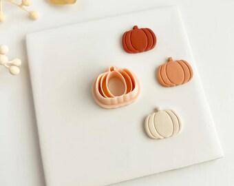 May include: An assortment of pumpkin-shaped items in various shades of orange and cream. The collection includes a pumpkin-shaped cookie cutter and three individual pumpkins, perfect for fall-themed crafts or baking.