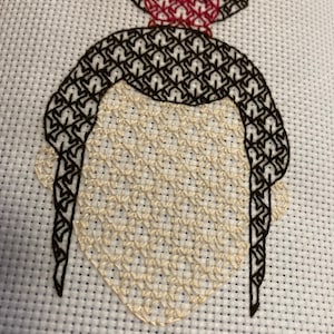 May include: Cross-stitch embroidery of a person's face with a red and white crown on top of their head. The face is stitched in beige thread, the hair is stitched in black thread, and the crown is stitched in red and white thread.